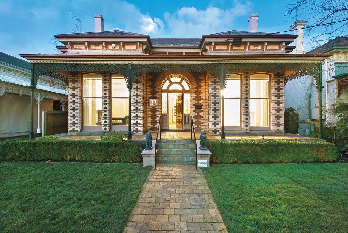 The front of the clinic: a restored red-brick period house with a verandah, iron lacework and a tiled path, at dusk